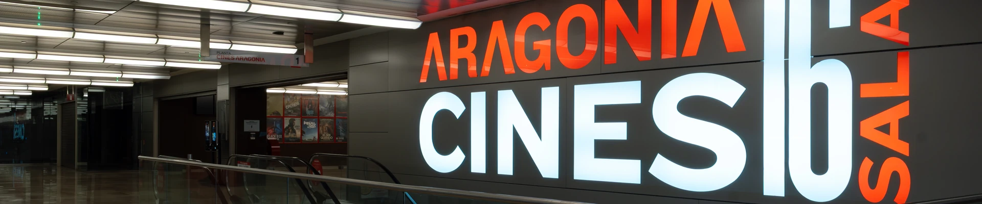 Acceso a los Cines Aragonia (16 salas) en el centro comercial Aragonia, con el gran rótulo iluminado, las escaleras mecánicas y los carteles de películas