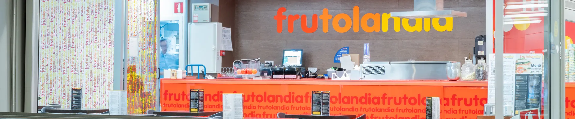 Local de zumos y sandwiches Frutolandia en el centro comercial Aragonia, con la barra naranja, la zona de preparación de zumos con fruta fresca y las mesas