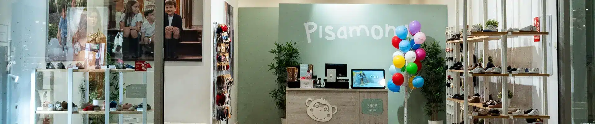 Interior de la zapatería infantil Pisamonas en el centro comercial Aragonia, con expositores de calzado para niños, mostrador con el logo del mono y globos